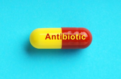 Capsule with word Antibiotic on light blue background, top view