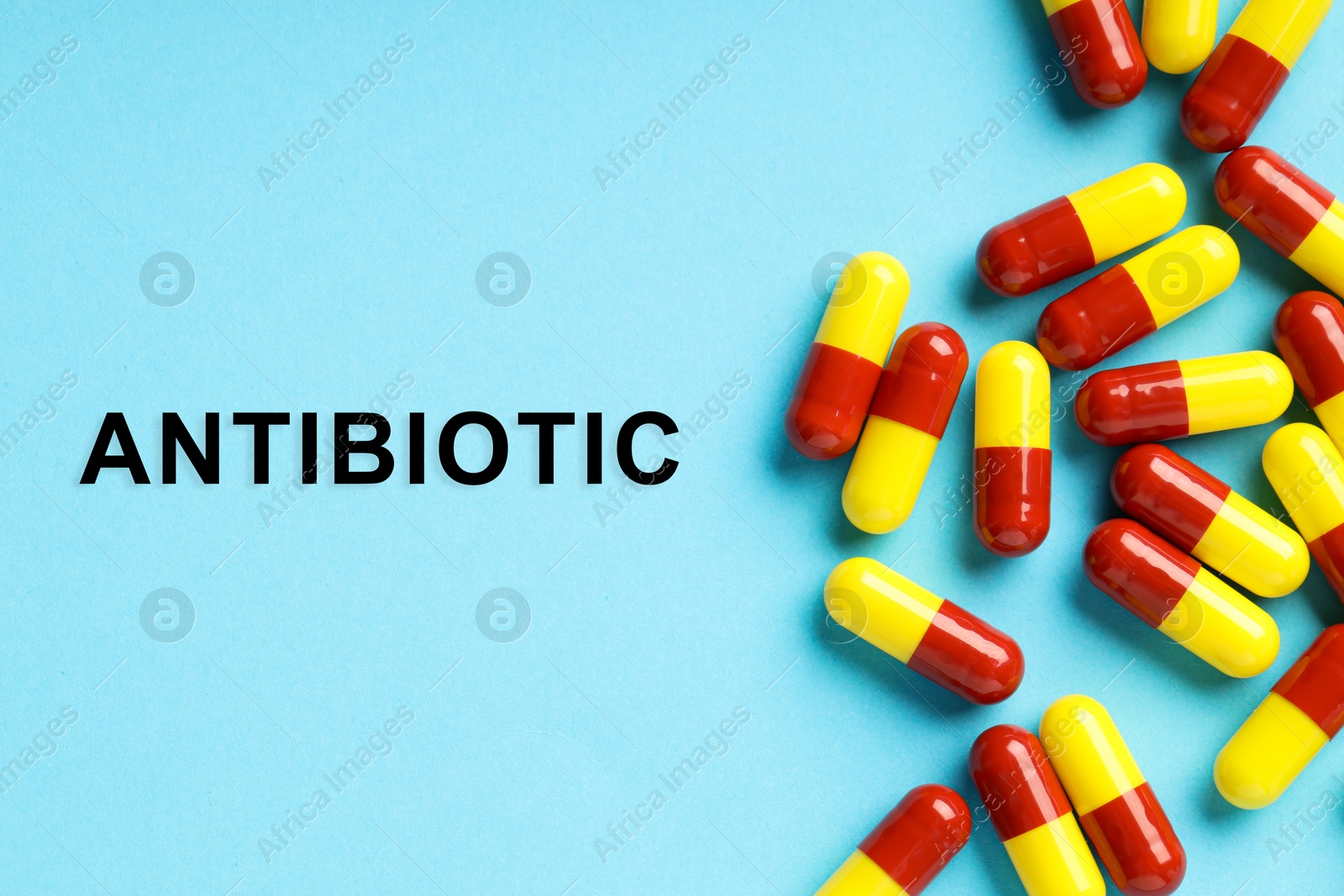 Image of Word Antibiotic and pills on light blue background, top view