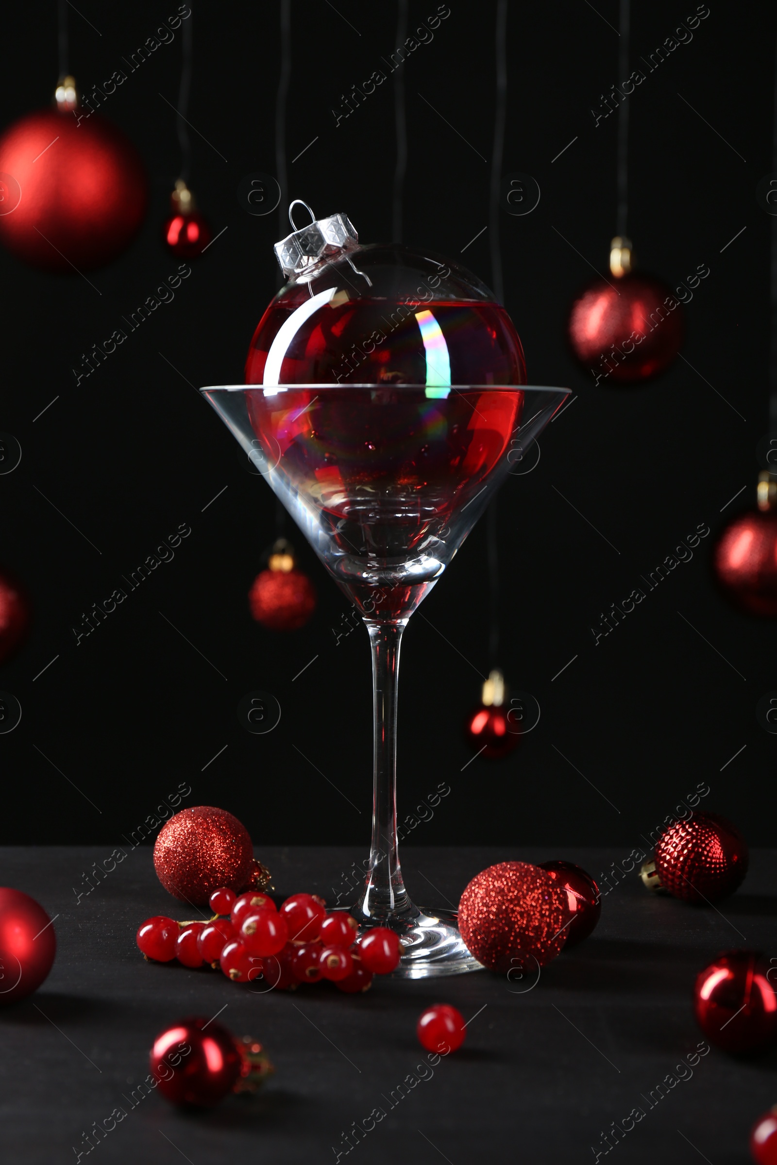 Photo of Creative presentation of Christmas cocktail in bauble and glass on black table