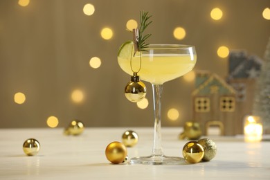 Photo of Tasty Christmas cocktail in glass and decor on white table against dark beige background with blurred lights. Space for text