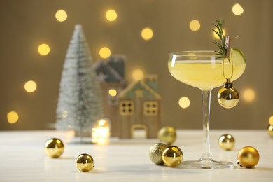 Photo of Tasty Christmas cocktail in glass and decor on white table against dark beige background with blurred lights. Space for text