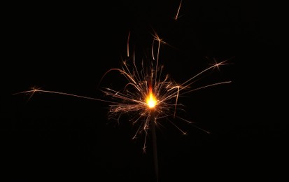 Photo of Burning sparkler stick on black background, space for text