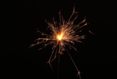 Photo of Burning sparkler stick on black background, space for text