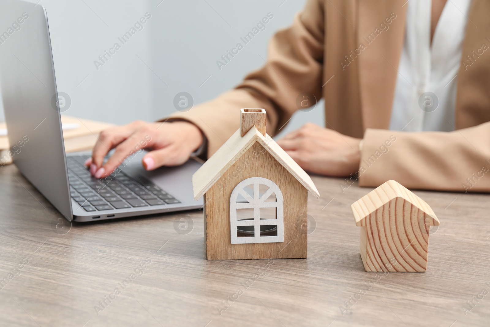 Photo of House hunting. Woman with laptop and house figures at wooden table, closeup