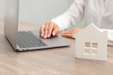 Photo of House hunting. Woman with laptop and house figure at wooden table, closeup