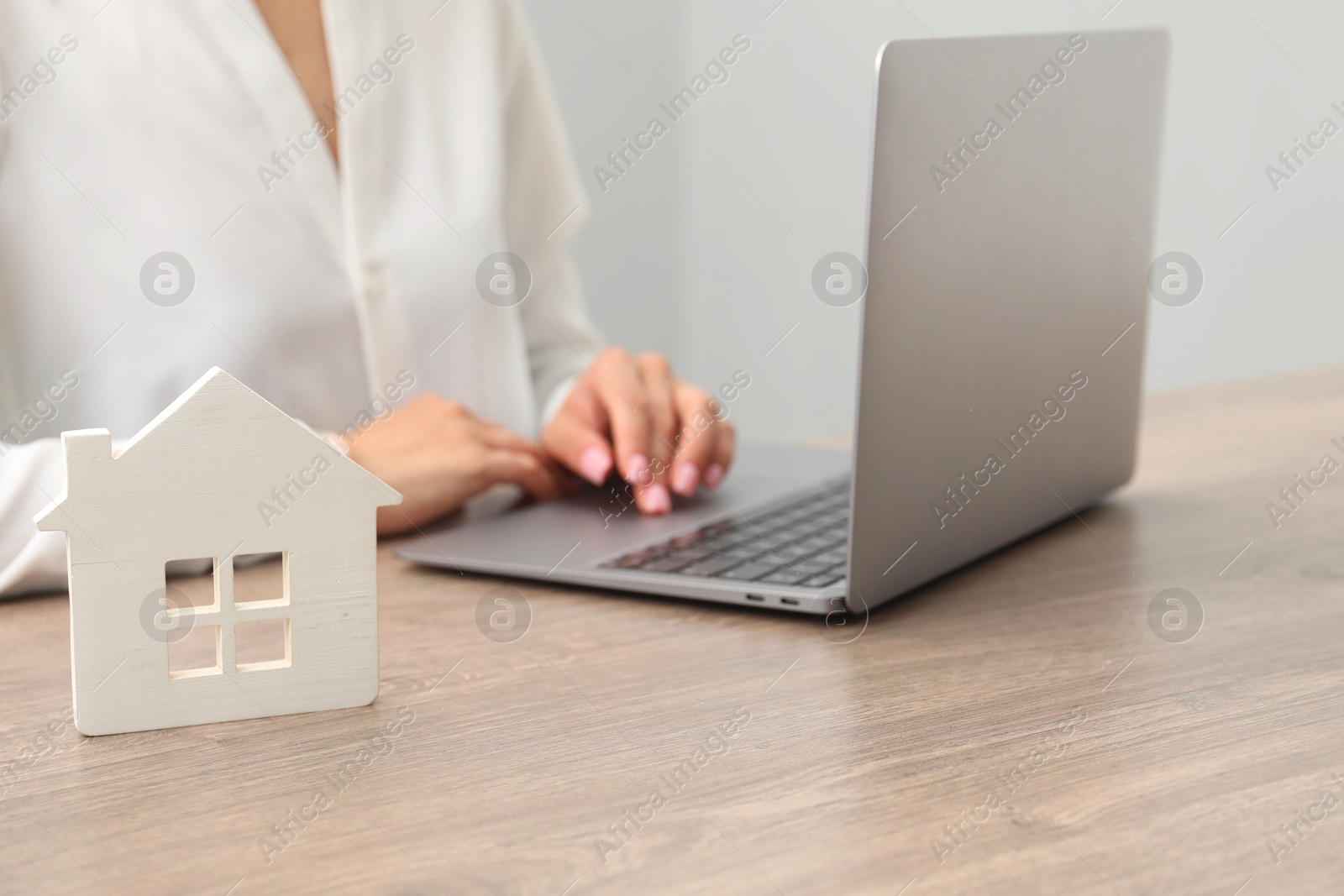 Photo of House hunting. Woman with laptop and house figure at wooden table, closeup