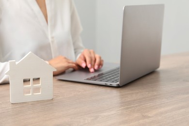 Photo of House hunting. Woman with laptop and house figure at wooden table, closeup