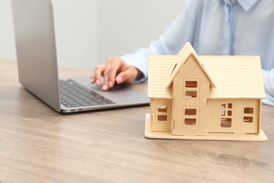 Photo of House hunting. Woman with laptop and house figure at wooden table, closeup