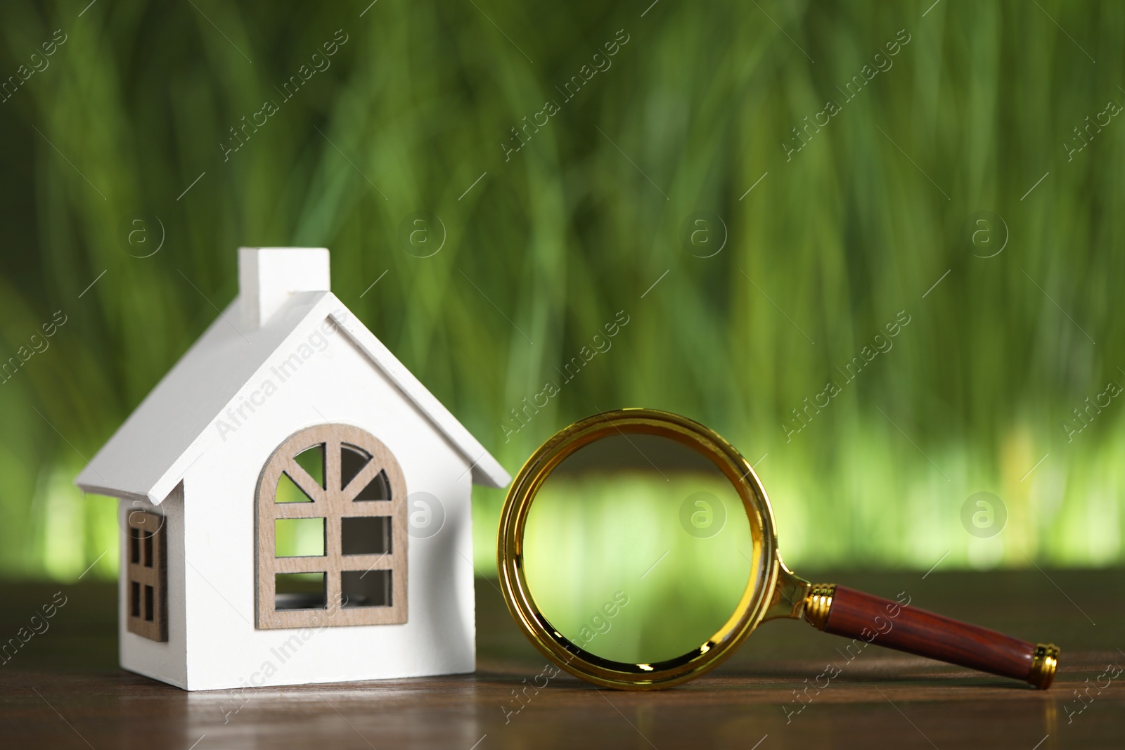 Photo of House hunting. Magnifying glass and house figure on wooden table