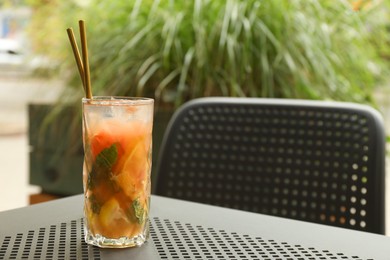 Photo of Glass of tasty refreshing drink and straws on table in outdoor cafe