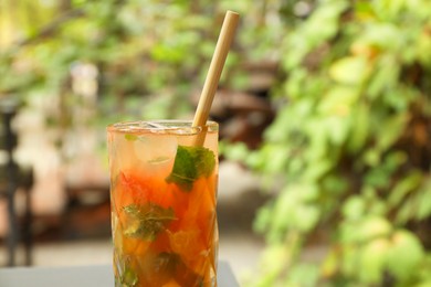 Photo of Glass of tasty refreshing drink and straw outdoors, closeup