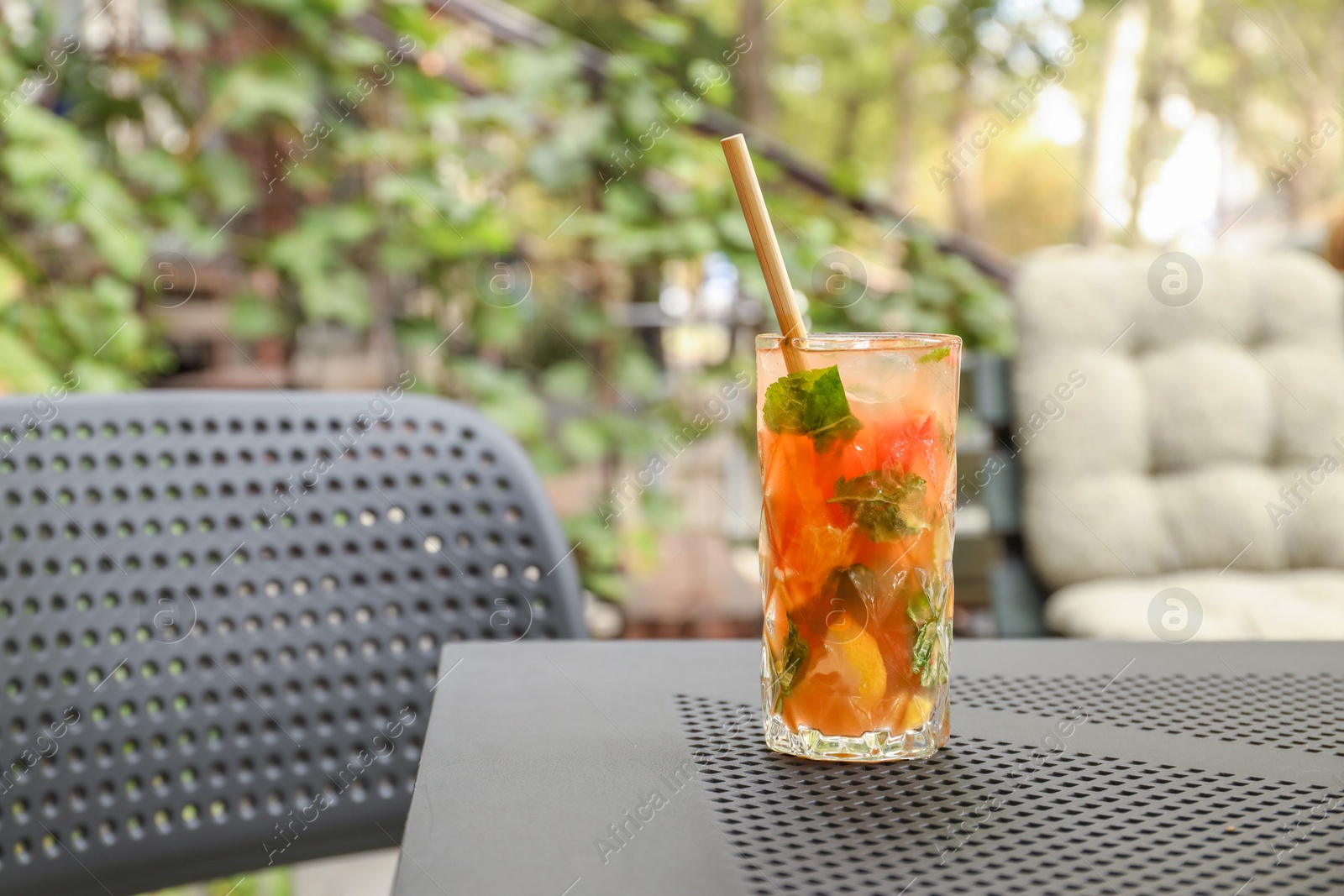 Photo of Glass of tasty refreshing drink and straw on table in outdoor cafe