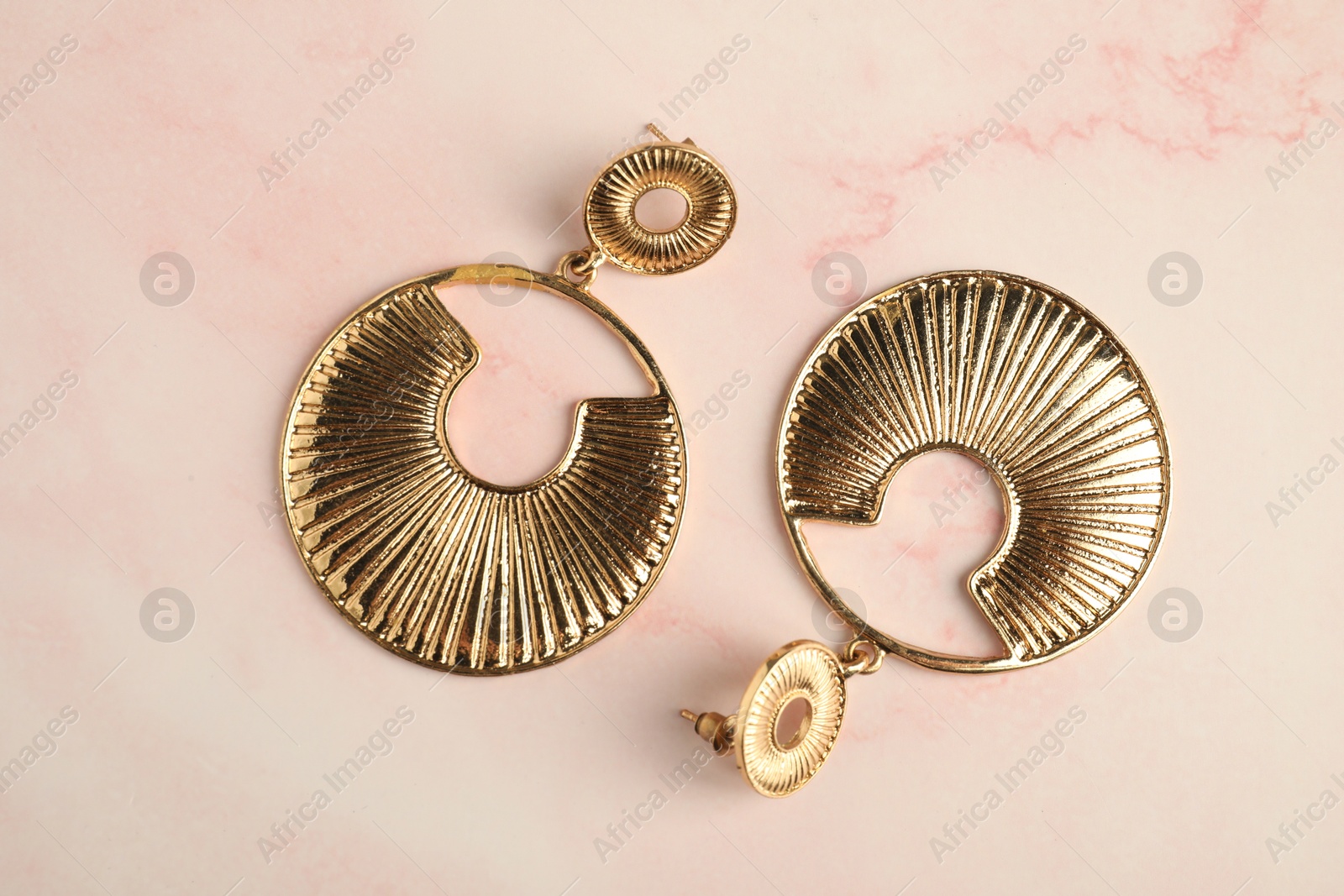 Photo of Beautiful bijouterie. Stylish earrings on light pink background, top view