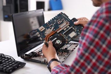 Photo of Man installing motherboard into laptop at white table, closeup