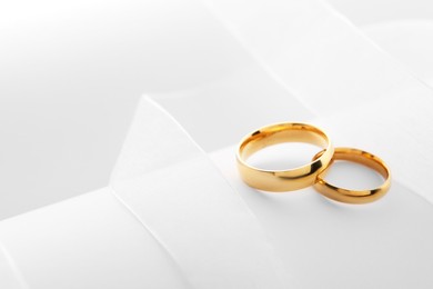 Photo of Beautiful golden wedding rings and white ribbon on light background