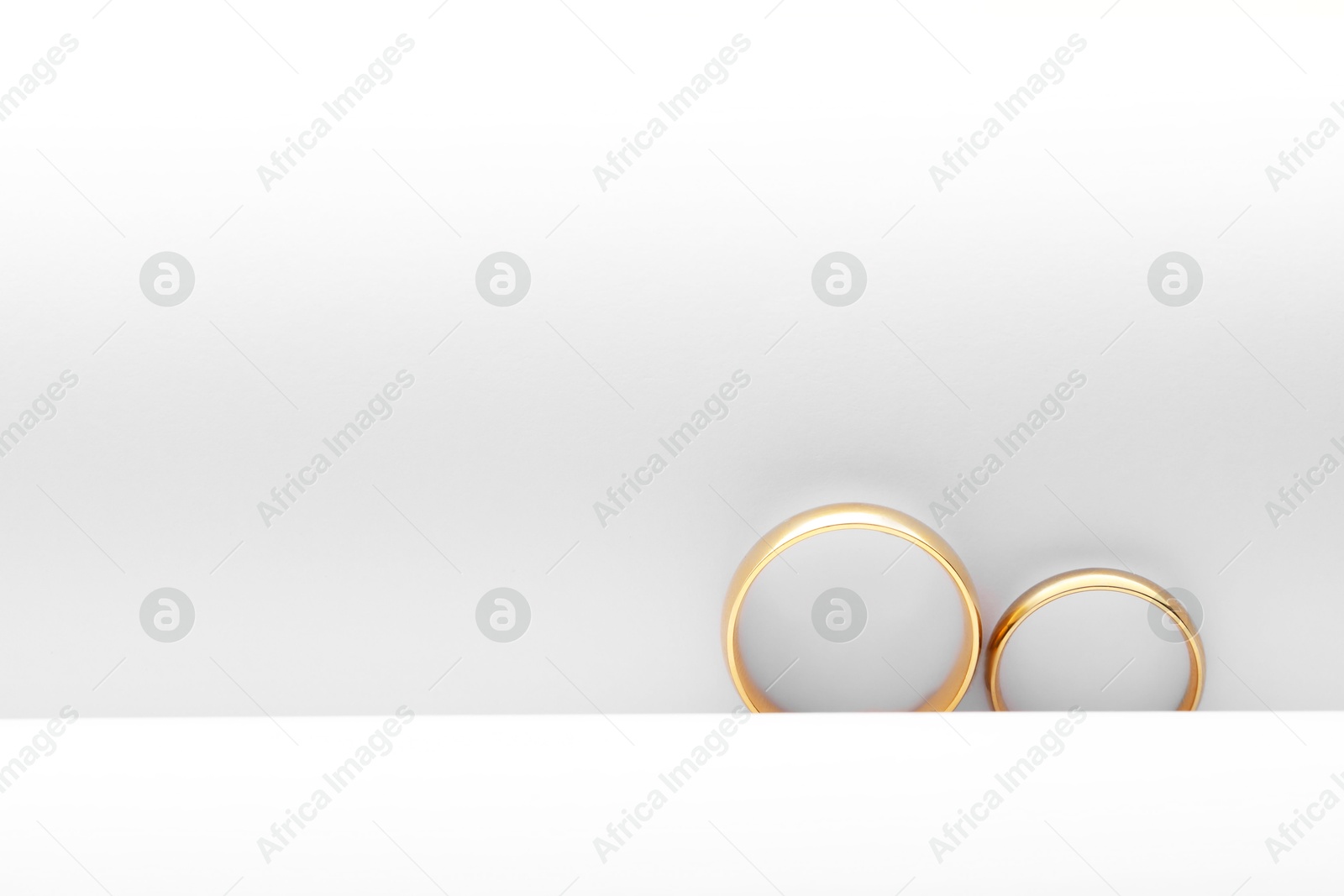 Photo of Beautiful golden wedding rings on white background, top view. Space for text