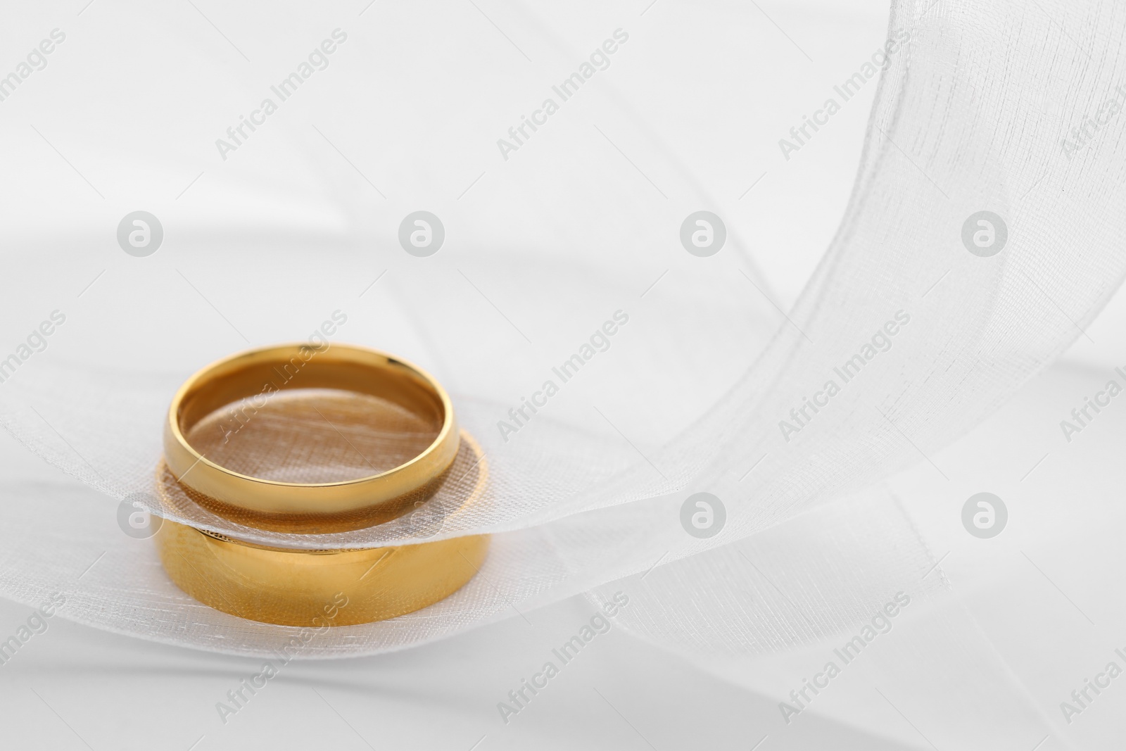 Photo of Beautiful golden wedding rings and ribbon on white background