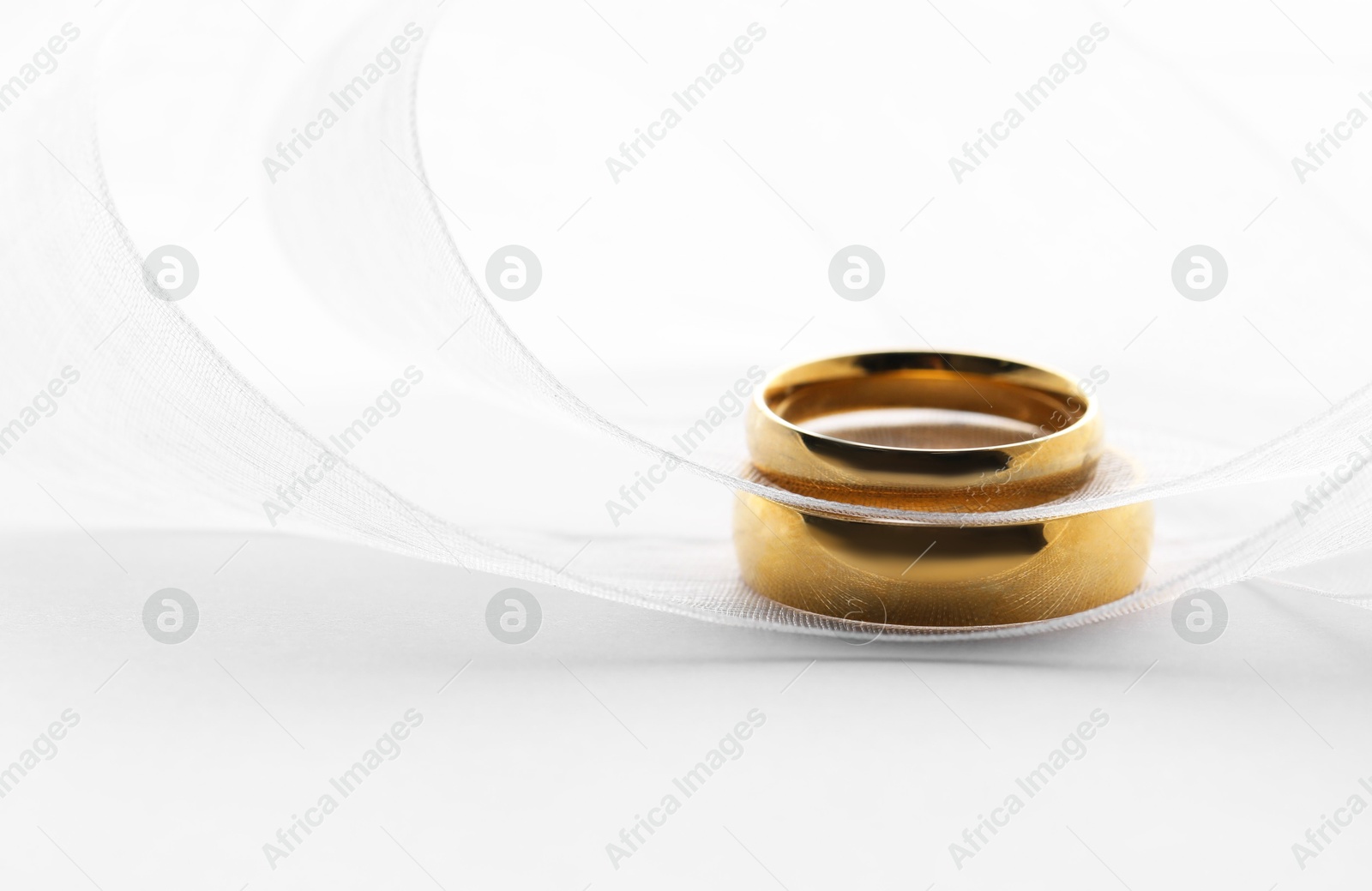 Photo of Beautiful golden wedding rings and ribbon on white background