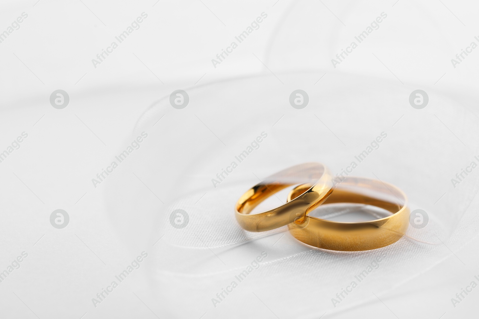 Photo of Beautiful golden wedding rings and ribbon on white background, closeup