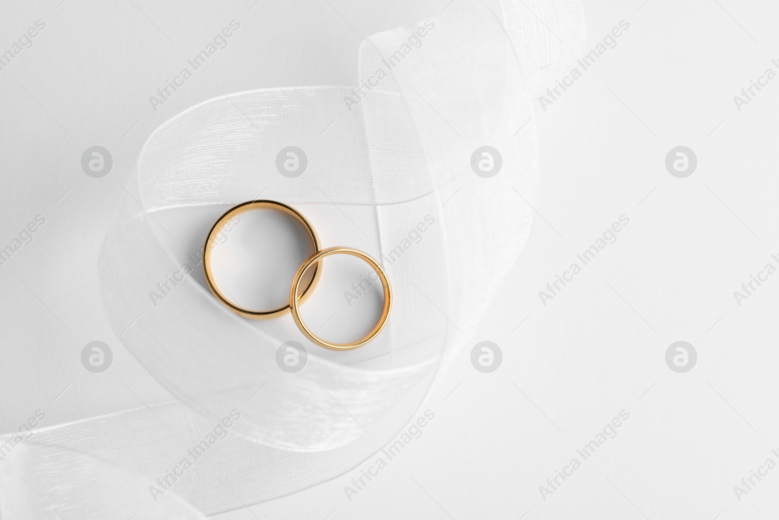 Photo of Beautiful golden wedding rings and ribbon on white background, top view