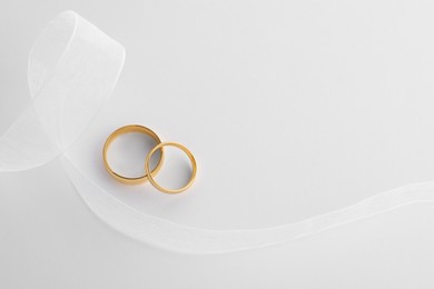 Photo of Beautiful golden wedding rings and ribbon on white background, flat lay. Space for text