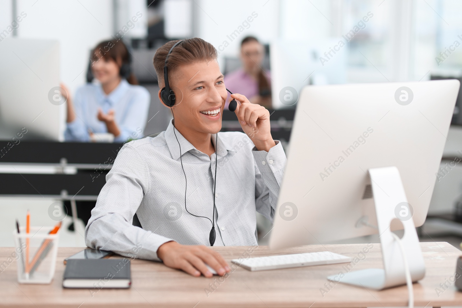 Photo of Salesman talking to client via headset at desk in office