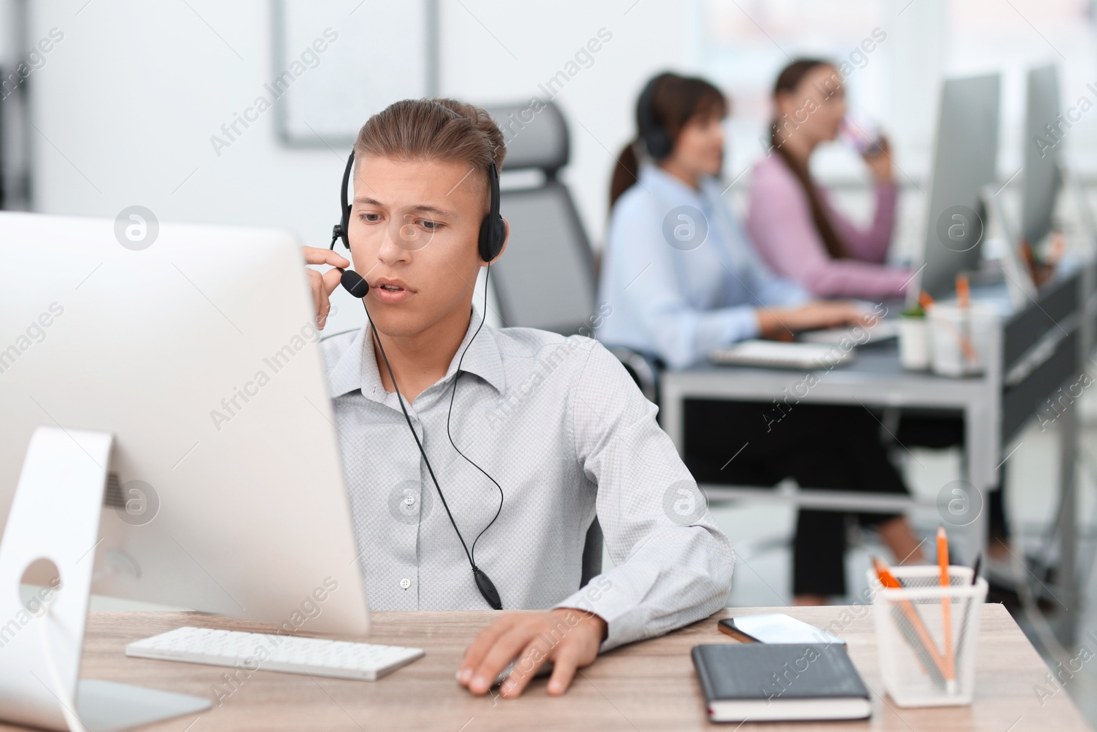 Photo of Salesman talking to client via headset at desk in office