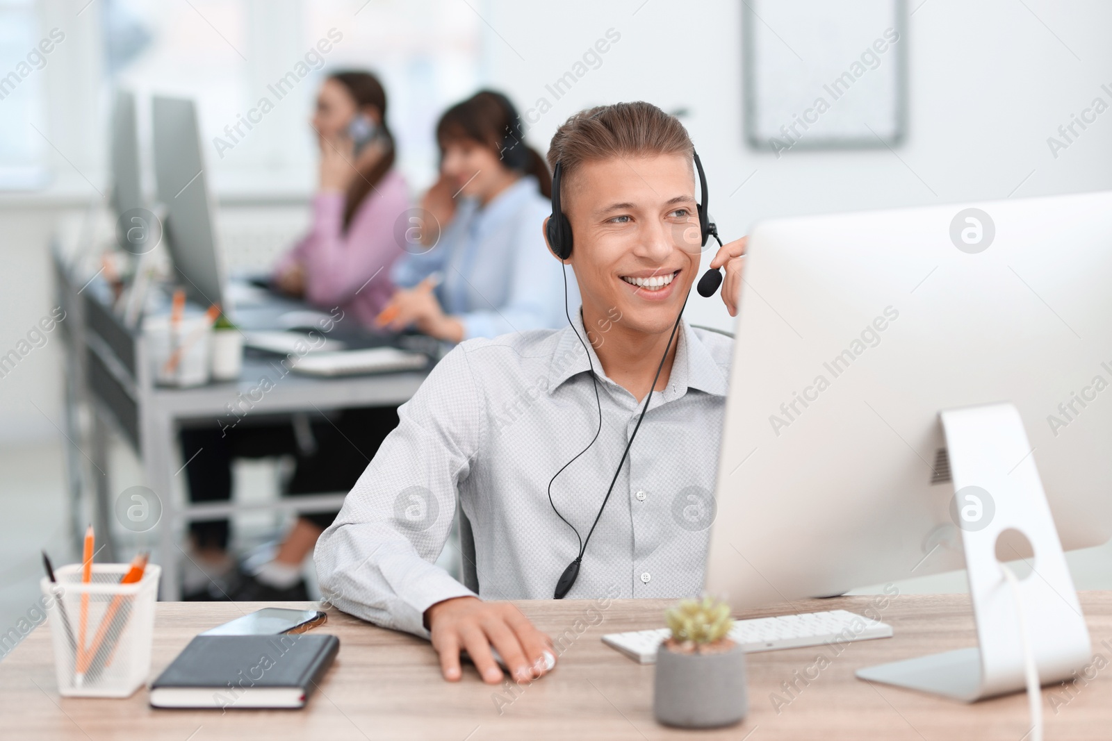 Photo of Salesman talking to client via headset at desk in office