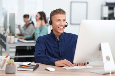 Photo of Salesman talking to client via headset at desk in office