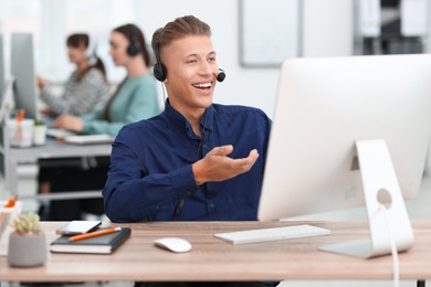 Photo of Salesman talking to client via headset at desk in office