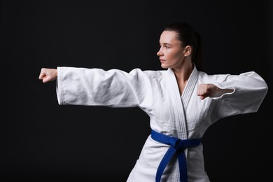 Photo of Young woman in kimono practicing karate on black background