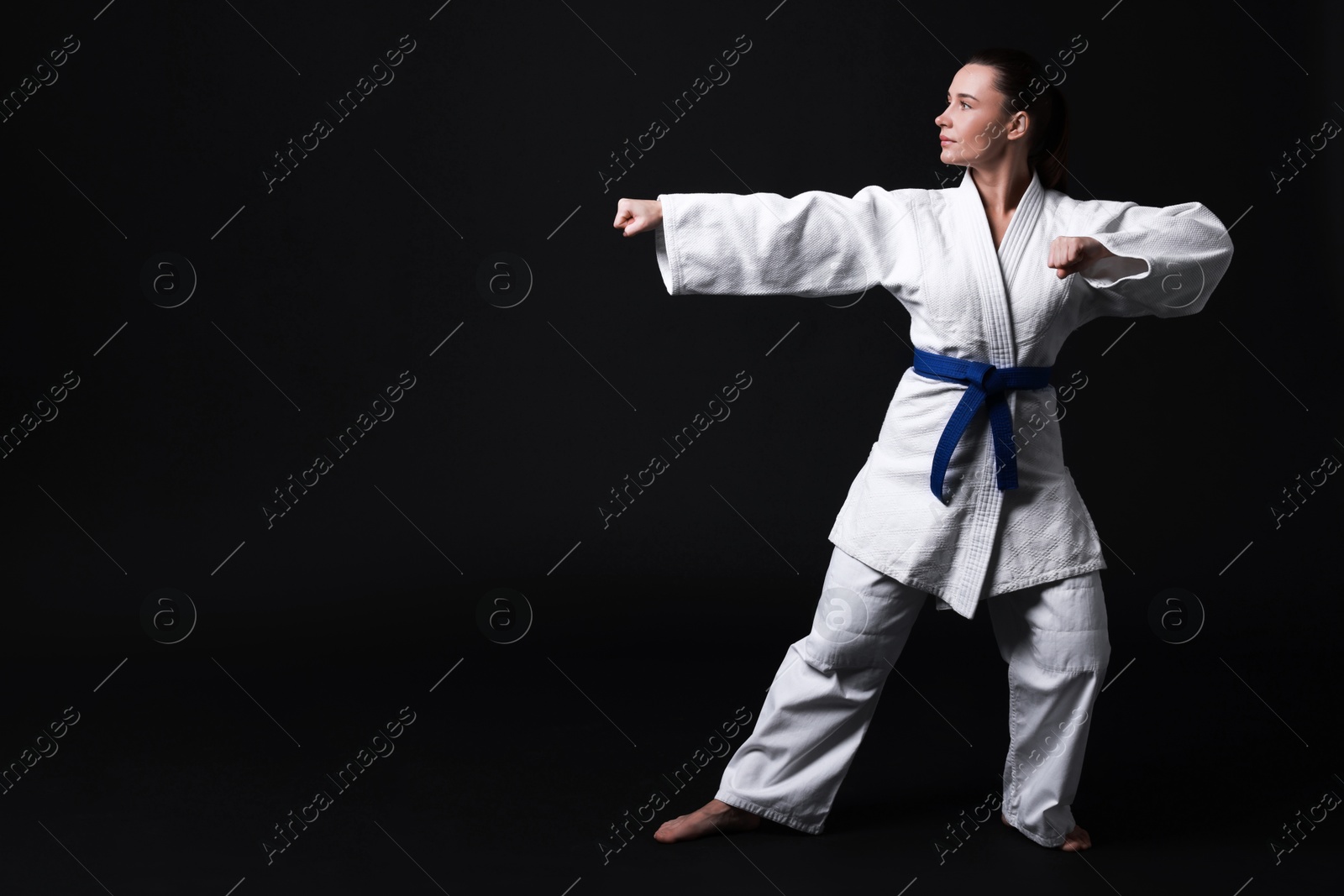 Photo of Young woman in kimono practicing karate on black background, space for text