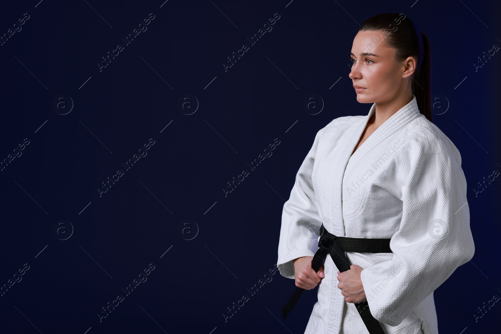 Photo of Karate fighter in kimono on dark background, space for text