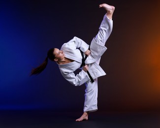 Photo of Young woman in kimono practicing karate on dark background