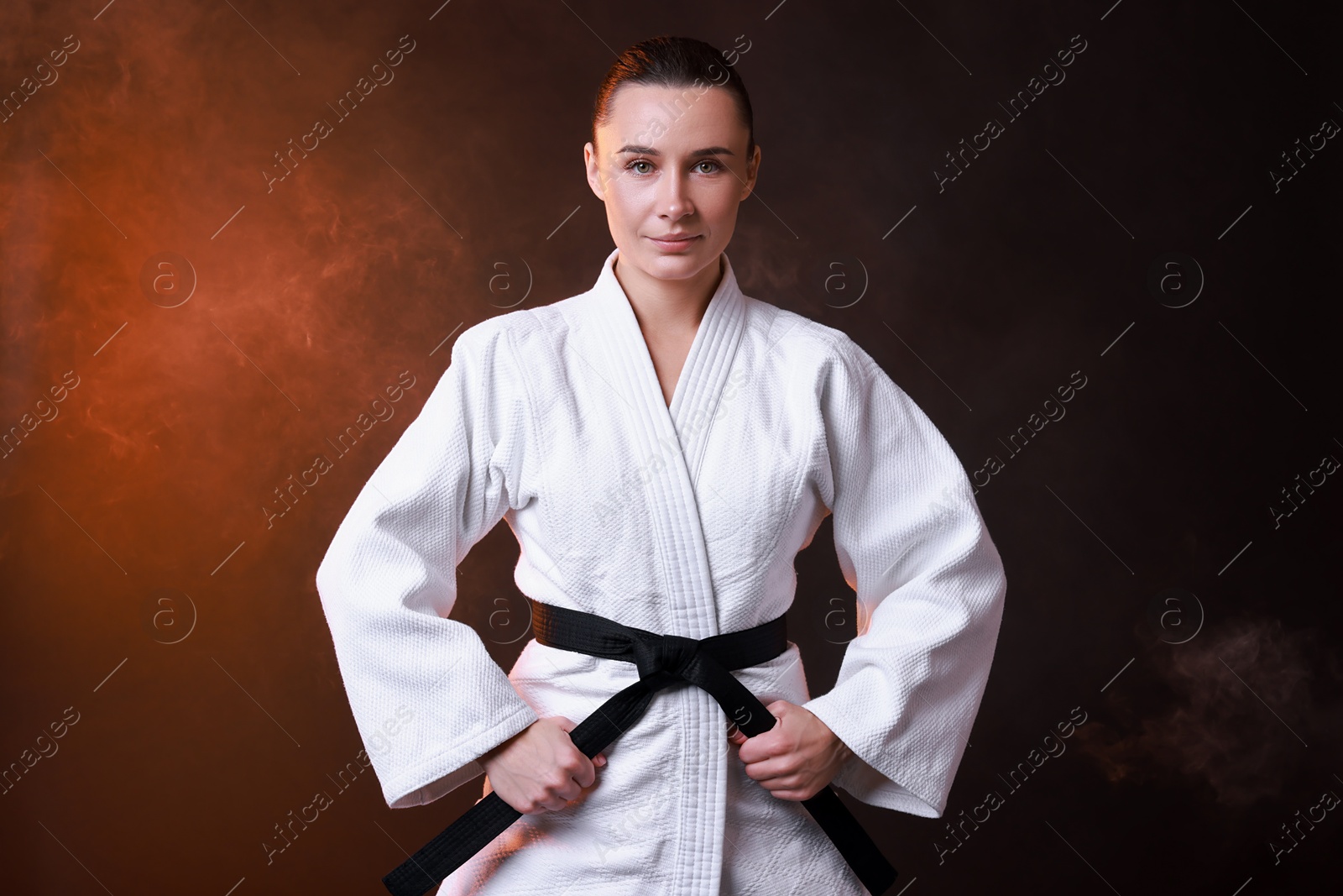 Photo of Young woman in kimono practicing karate on dark background