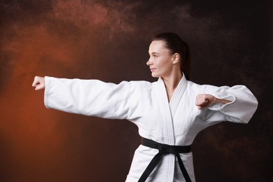 Photo of Young woman in kimono practicing karate on dark background