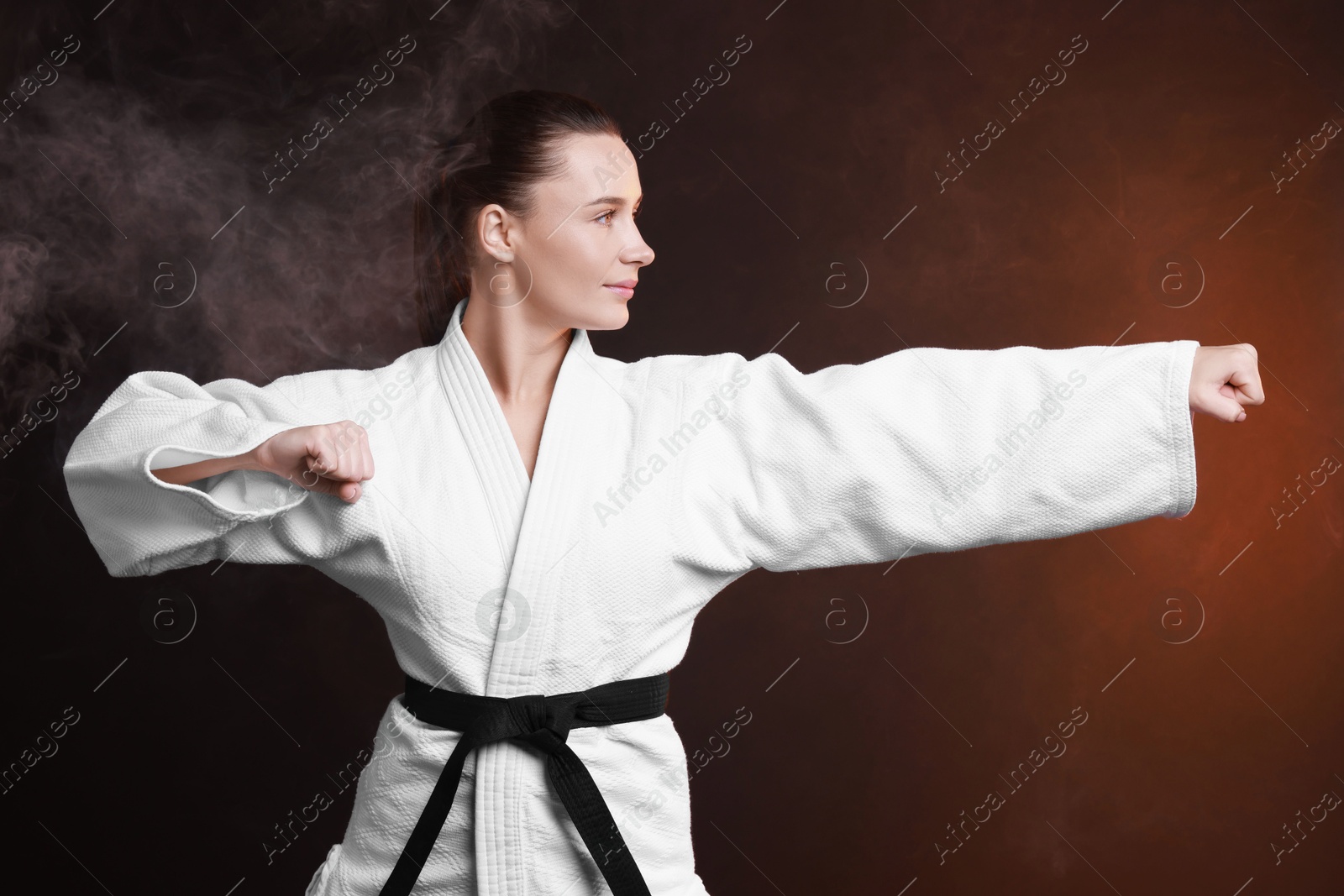 Photo of Young woman in kimono practicing karate on dark background