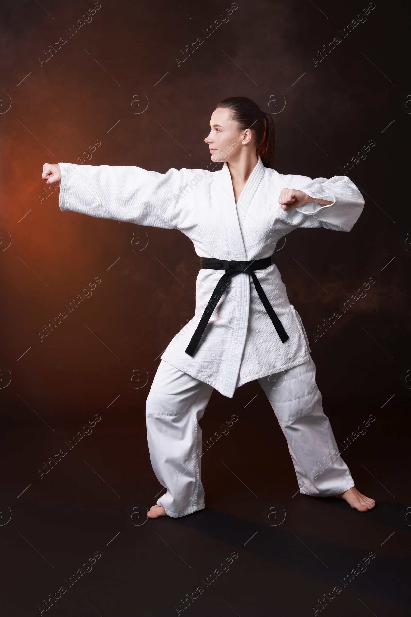 Photo of Young woman in kimono practicing karate on dark background