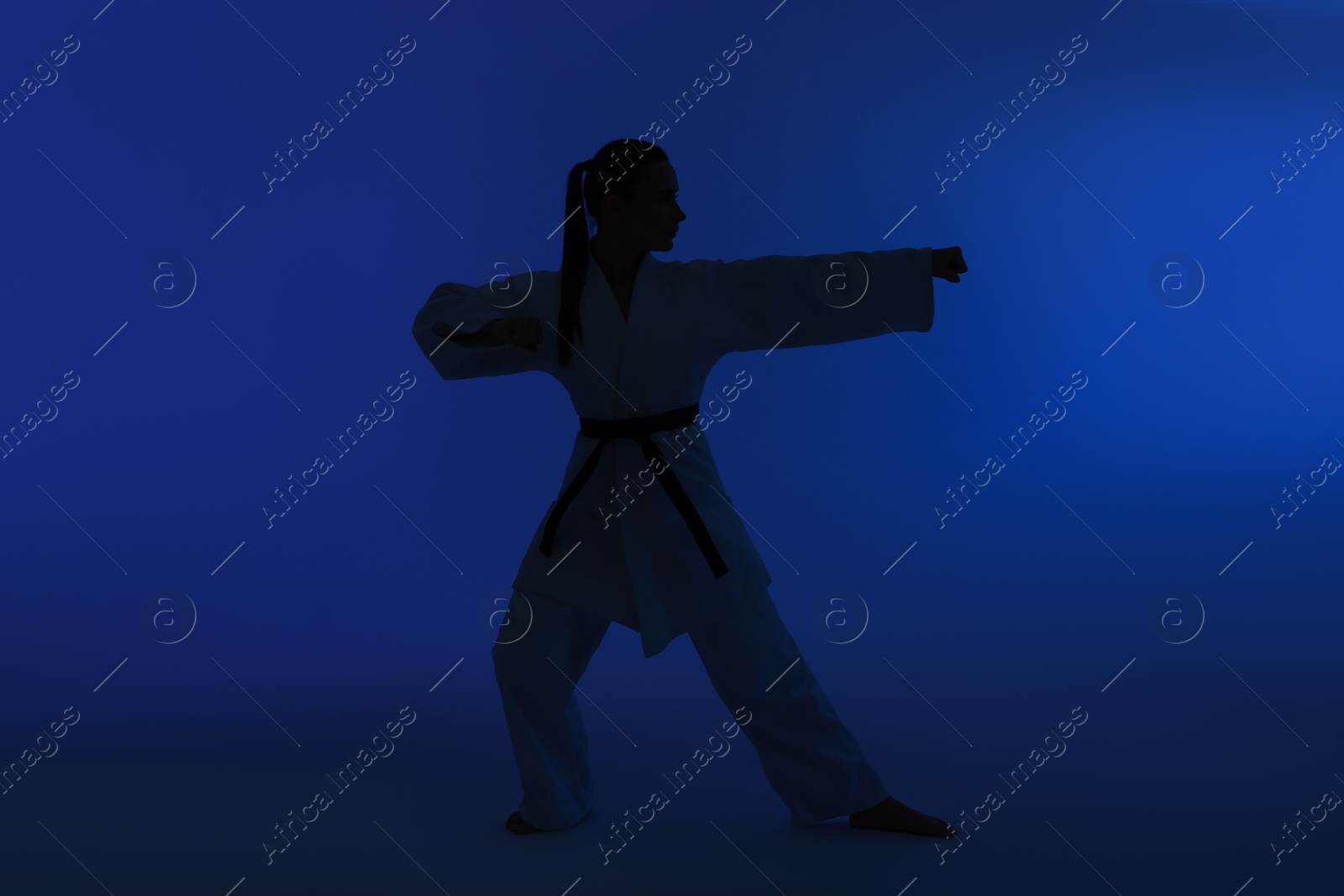 Photo of Silhouette of woman in kimono practicing karate on dark blue background