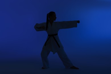 Photo of Silhouette of woman in kimono practicing karate on dark blue background