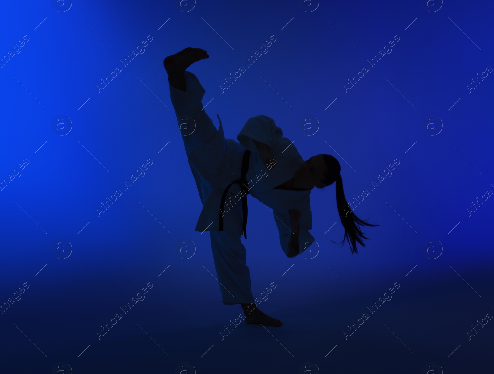 Photo of Silhouette of woman in kimono practicing karate on dark blue background