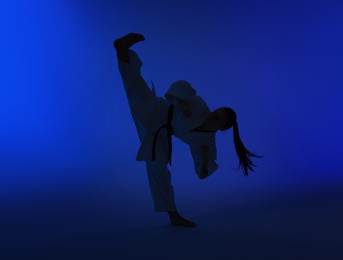 Silhouette of woman in kimono practicing karate on dark blue background