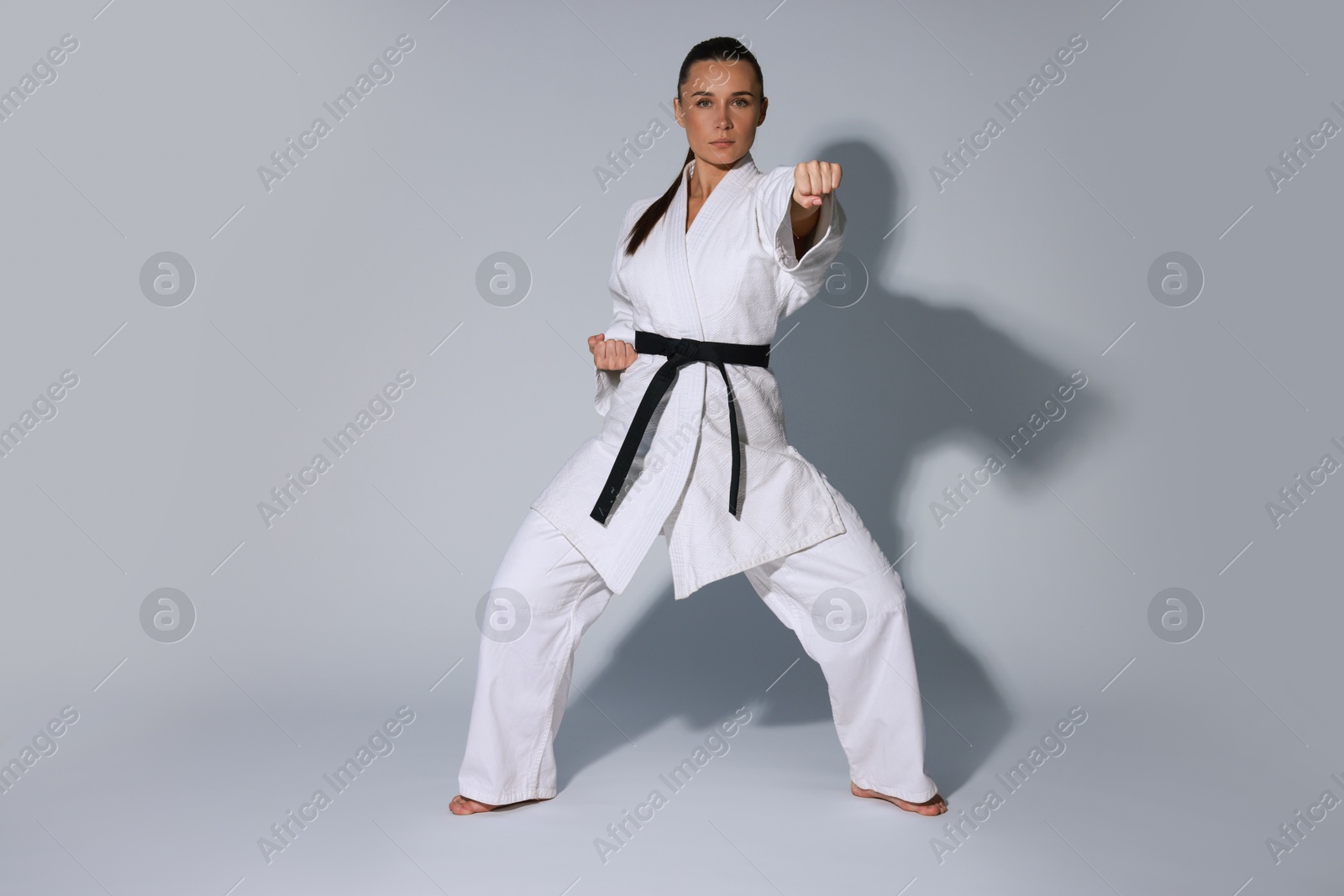 Photo of Young woman in kimono practicing karate on grey background