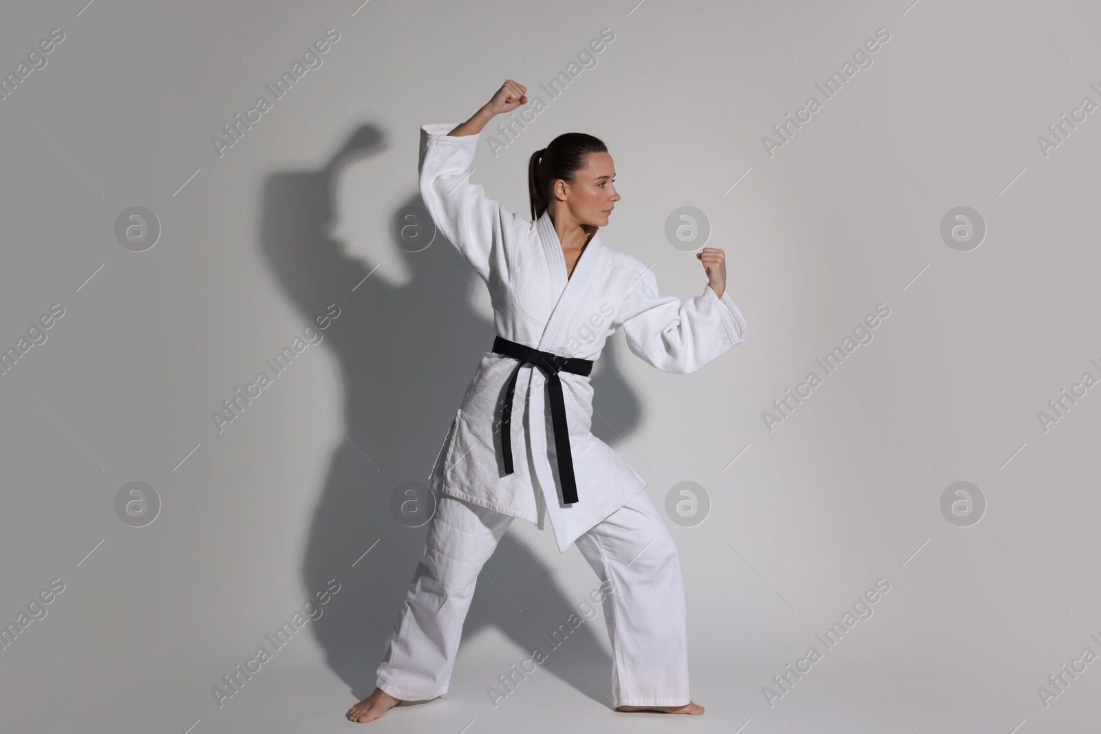 Photo of Young woman in kimono practicing karate on grey background, space for text