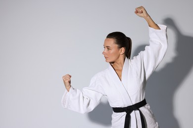 Photo of Young woman in kimono practicing karate on grey background, space for text