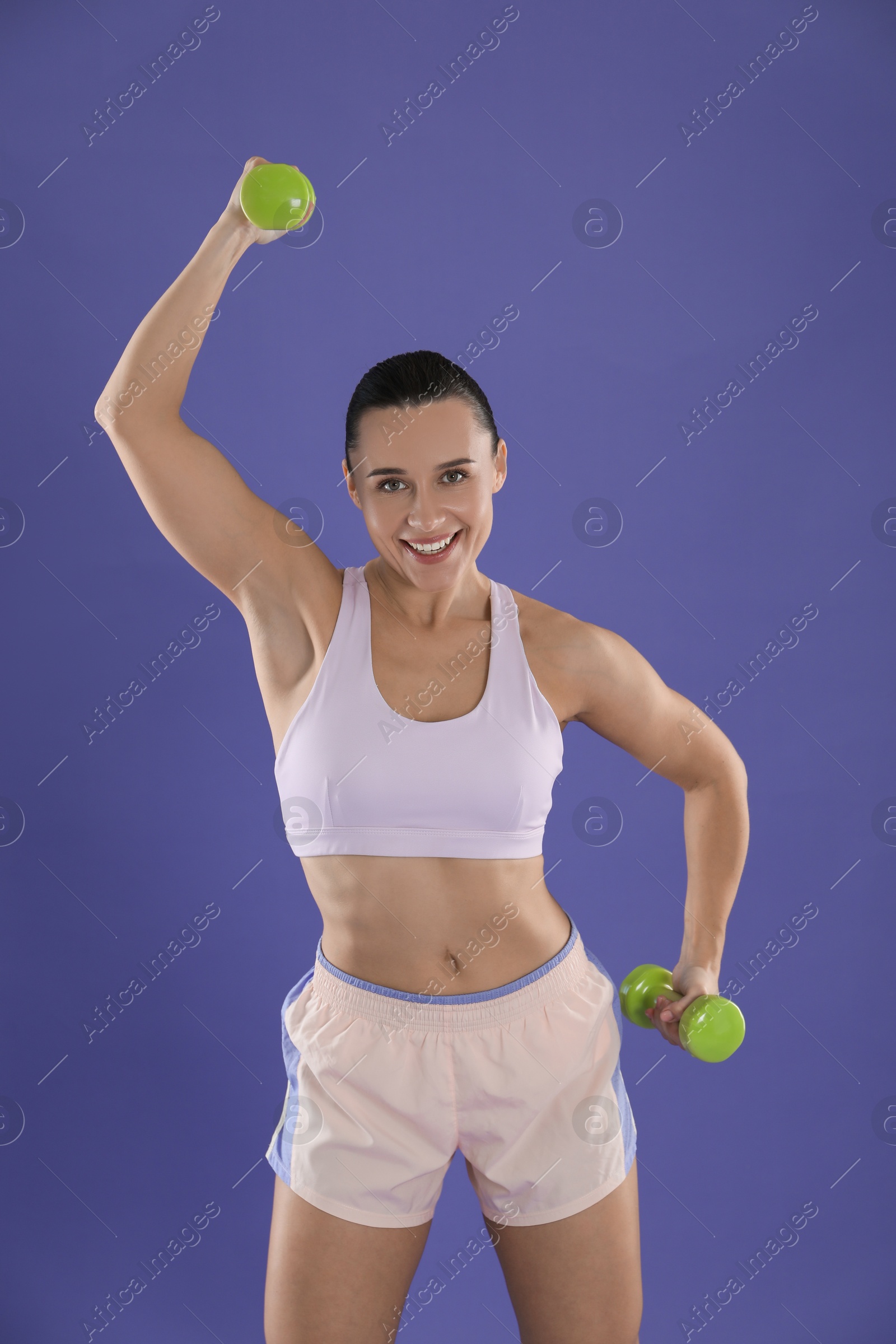 Photo of Woman exercising with dumbbells on purple background