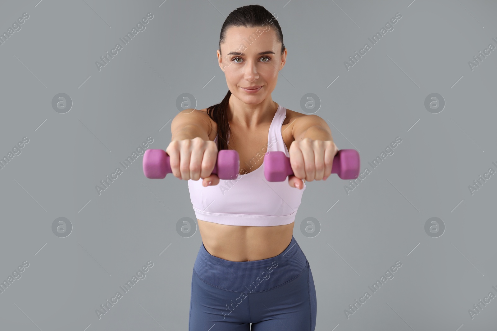 Photo of Woman exercising with dumbbells on light grey background