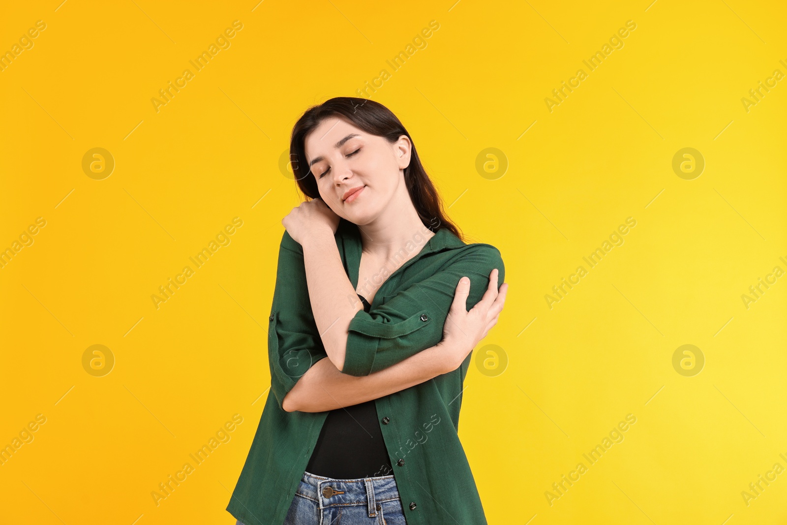 Photo of Beautiful young woman hugging herself on yellow background, space for text