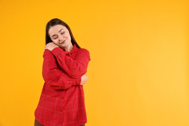 Photo of Beautiful young woman hugging herself on yellow background, space for text