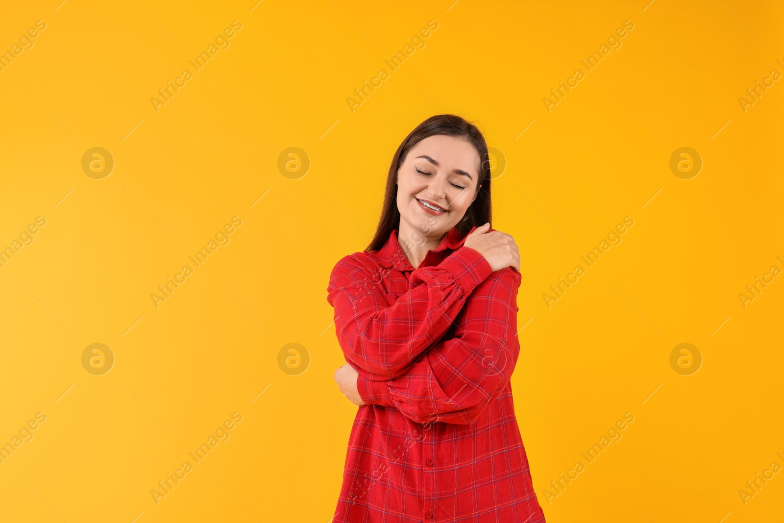 Photo of Beautiful young woman hugging herself on yellow background